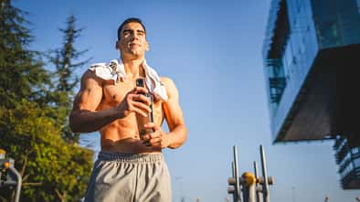 Ein trainierter, oberkörperfreier Mann hält einen Shaker in der Hand 