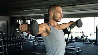 Mann trainiert Schultern mit Kurzhanteln im Gym
