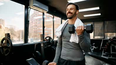 Junger Sportler, der mit Kurzhanteln im Fitnessstudio trainiert
