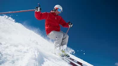 Ein Mann fährt bei blauem Himmel im Schnee eine Ski-Piste herunter