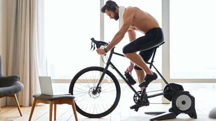 Indoor Cycling, Spinning, Bike, Rennrad, Rolle, Fahrrad, Indoor Sport Muskulöser Mann radelt im Wohnzimmer auf seinem Rennrad in einer Rolle