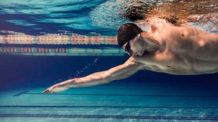 Schwimmen Mann mit schwarzer Badekappe schwimmt Kraul und wird unter Wasser fotografiert.