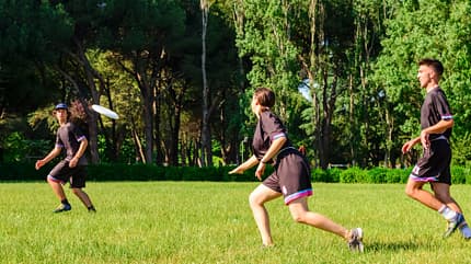 ultimate frisbee Zwei Männer und eine Frau in Sportkleidung spielen auf dem Rasen mit einer Frisbee.