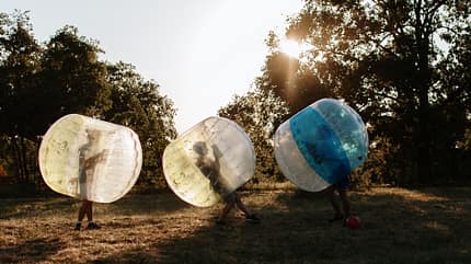 bubble ball Drei Personen stecken in großen, transparenten Bällen und laufen über eine Wiese im Sonnenuntergang.