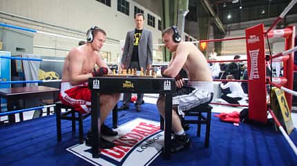 schachboxen Zwei Männer in Boxshorts sitzen in einem Boxring an einem Schachbrett.