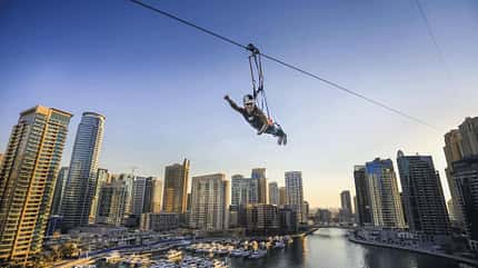 Ein Mann hängt an einer Zipline, die quer über den Hafen von Dubai gespannt ist Ein Mann hängt an einer Zipline, die quer über den Hafen von Dubai gespannt ist