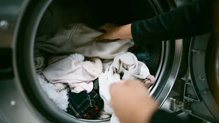 Kleidung in Waschmaschine legen / Frühling 2024 / Ana Rocio Garcia Franco / Getty Images Woman hands putting her dirty clothes in the washing machine in a laundromat