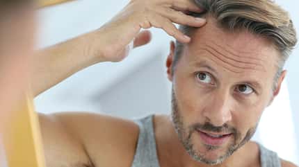 Mann schaut sich im Spiegel seine Haare an Mann schaut sich im Spiegel seine Haare an