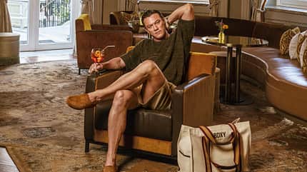Luke Evans sitzt auf einem Sessel, neben ihm eine Tasche seiner eigenen Modemarke Luke Evans sitzt auf einem Sessel, neben ihm eine Tasche seiner eigenen Modemarke
