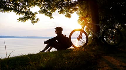 junger Mann sitzt mit seinem Fahrrad im Sonnenuntergang am See