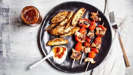 barbecue,chicken,cutlery,dip,dishes,gyros,home,meals,nobody,nutrition,overhead view,party,potato,ready to eat Gyros chicken skewers with tomatoes, bell peppers, potato wedges and tzatziki on table