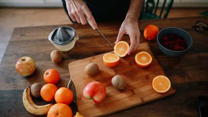 Mann, der zu Hause ein gesundes Frühstück zubereitet, Früchte für einen Smoothie in seiner Küche schneidet Mann, der zu Hause ein gesundes Frühstück zubereitet, Früchte für einen Smoothie in seiner Küche schneidet