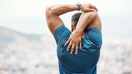Muskulöser männlicher Athlet, der sich aufwärmt, und seinen Arm hinter dem Rücken stretcht Muskulöser männlicher Athlet, der sich aufwärmt, und seinen Arm hinter dem Rücken stretcht