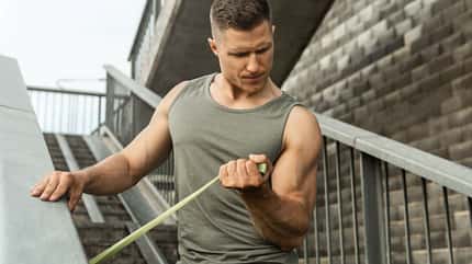Muskulöser Mann beim Training mit einem Widerstandsgummiband auf einer Straße Muskulöser Mann beim Training mit einem Widerstandsgummiband auf einer Straße