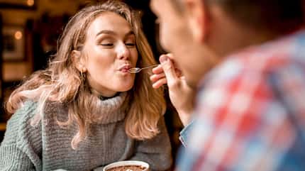 Junger Mann, der eine junge Frau in einem Café mit Milchschaum füttert Junger Mann, der eine junge Frau in einem Café mit Milchschaum füttert