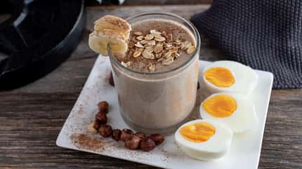 Schoko-Proteinshake im Glas mit gekochten Eiern daneben Schoko-Proteinshake im Glas mit gekochten Eiern daneben