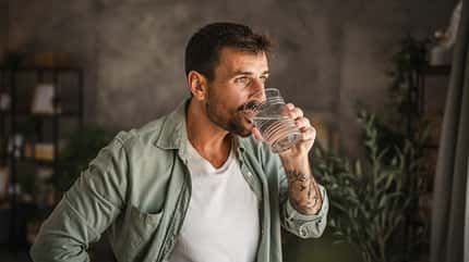 Mann trinkt ein Glas Wasser vor dunklem Hintergrund Mann trinkt ein Glas Wasser vor dunklem Hintergrund