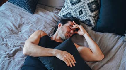 Mann ruht sich im Bett aus und drückt sich an den Augen Mann ruht sich im Bett aus und drückt sich an den Augen