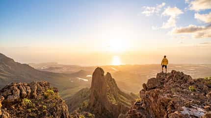 Mann betrachtet den Sonnenuntergang auf einem Berggipfel Mann betrachtet den Sonnenuntergang auf einem Berggipfel