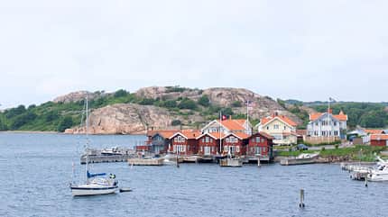 Landschaft in Schweden: Rote Häuser vor dem Wasser mit einem Segelboot Landschaft in Schweden: Rote Häuser vor dem Wasser mit einem Segelboot