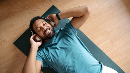 The single man exercising alone at home while listening to music through wireless headphones. Young man is happy, relaxed, and content with his life. Solo home workout and meditation, morning or evening workout routine. The single man exercising alone at home while listening to music through wireless headphones. Young man is happy, relaxed, and content with his life. Solo home workout and meditation, morning or evening workout routine.