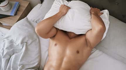 Mann liegt im Bett mit Bettdecke vor dem Kopf Mann liegt im Bett mit Bettdecke vor dem Kopf