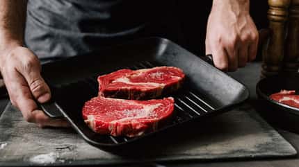 Mann kocht Rindersteaks mit einer Grillpfanne mit Rindersteaks auf Küche Mann kocht Rindersteaks mit einer Grillpfanne mit Rindersteaks auf Küche