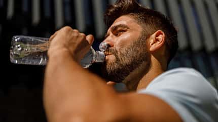 Nahaufnahme eines Sportlers, der Wasser aus der Flasche trinkt, nachdem er im Hintergrund der Wolkenkratzer der Stadt gelaufen ist 