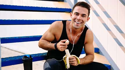 Smiling,Sporty,Guy,In,Earphones,,Eating,A,Banana,,After,Workout,