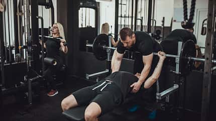 Fitnesslehrer hilft beim Bankpresstraining 