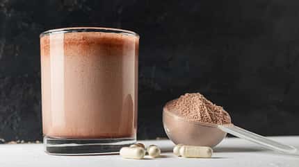 Schokoladen-Proteinshake in einem Glas mit einem Messlöffel Proteinpulver Schokoladen-Proteinshake in einem Glas mit einem Messlöffel Proteinpulver