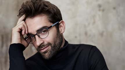 Ein Mann mit Brille, der sich die Hand an die Schläfe legt