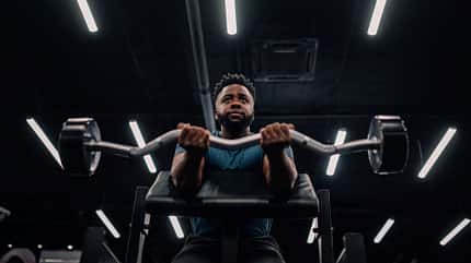 Ein junger Mann führt Scott-Curls aus an der Maschine im Gym