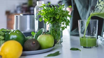 Glas mit grünem Smoothie und Zutaten für diesen im Vordergrund Glas mit grünem Smoothie und Zutaten für diesen im Vordergrund