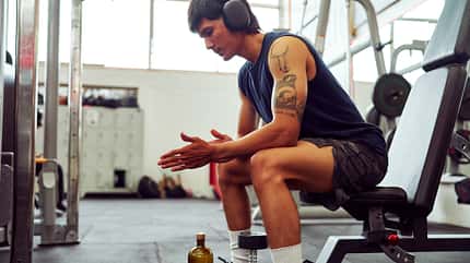 Young sportsman wearing headphones resting on bench in gym after workout Young sportsman wearing headphones resting on bench in gym after workout