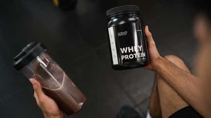 Ein Mann sitzt nach dem Training auf einer Bank und trinkt einen Whey-Shake Ein Mann sitzt nach dem Training auf einer Bank und trinkt einen Whey-Shake