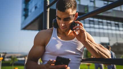 Ein Mann schaut auf sein Smartphone und greift sich an seine Kopfhörer Ein Mann schaut auf sein Smartphone und greift sich an seine Kopfhörer