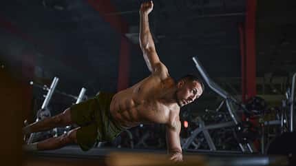 Muscular build men exercising endurance in side plank pose in a gym. Muscular build men exercising endurance in side plank pose in a gym.