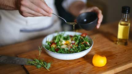 Ein Mann verteilt Essig über einem Salat Ein Mann verteilt Essig über einem Salat