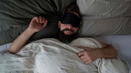 Ein Mann liegt mit Schlafmaske im Bett