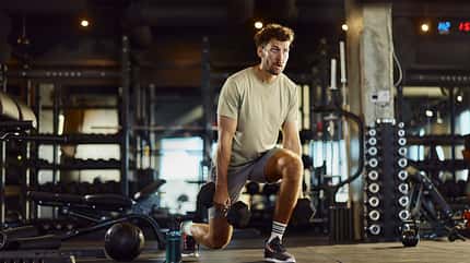 Determined male athlete exercising lunges with weights in a gym.