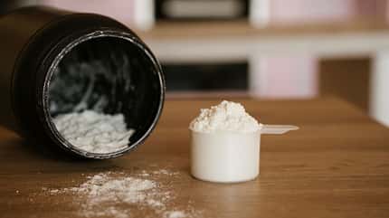 Eine Dose Proteinpulver mit einem Scoop voll mit Pulver davor  Eine Dose Proteinpulver mit einem Scoop voll mit Pulver davor