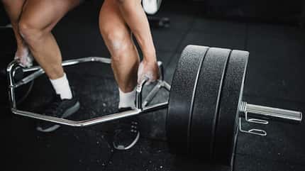 Nahaufnahme der Beine eines Mannes der beim Kreuzheben die Langhantel anhebt Nahaufnahme der Beine eines Mannes der beim Kreuzheben die Langhantel anhebt