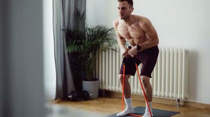 Ein muskulöser Mann trainiert zuhause mit einem Resistance Band Ein muskulöser Mann trainiert zuhause mit einem Resistance Band