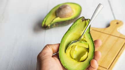 Ein Hand hält eine Avocado, ein Löffel steckt im Fruchtfleisch Ein Hand hält eine Avocado, ein Löffel steckt im Fruchtfleisch