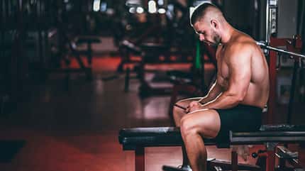 Ein trainierter Mann sitzt auf einer Hantelbank und schaut auf sein Smartphone