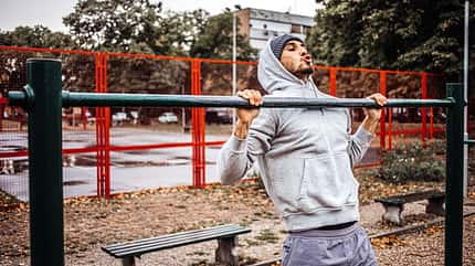 Young men in a gray tracksuit on an autumn rainy day exercising on a gymnastic device in a public park