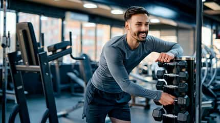 Ein trainierter Mann greift nach Kurzhanteln Ein trainierter Mann greift nach Kurzhanteln