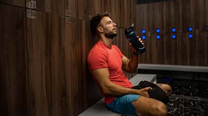 Tired athletic man drinking water and resting in locker room. Tired athletic man drinking water and resting in locker room.