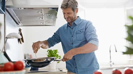 Mature man in his kitchen frying vegetables